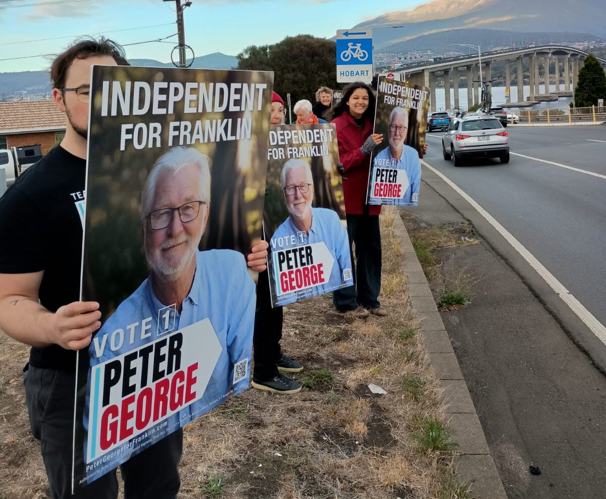 Three volunteers hold Peter George corflutes in front of the Tasman Bridge. The corflutes say Independent for Franklin Vote 1 Peter George.
